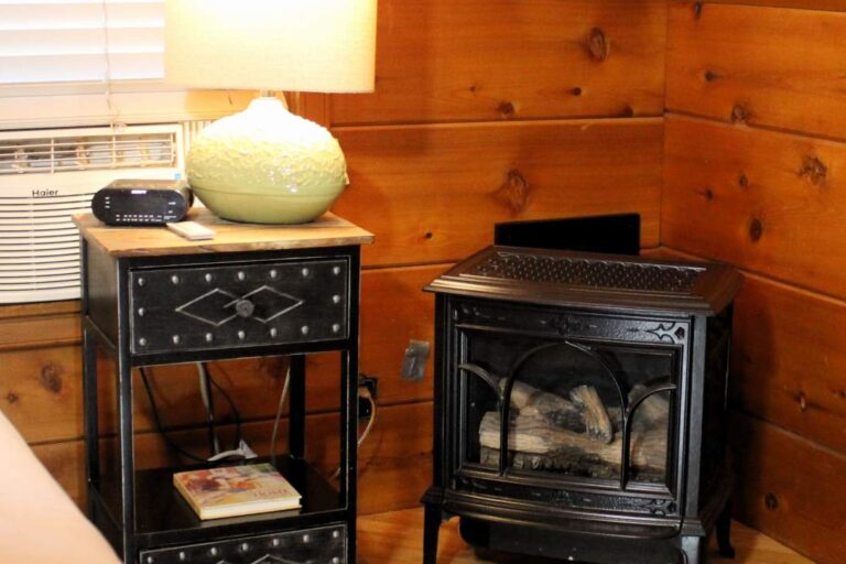 Classic black cast iron gas fireplace stove in the corner of a wood-paneled cabin bedroom.