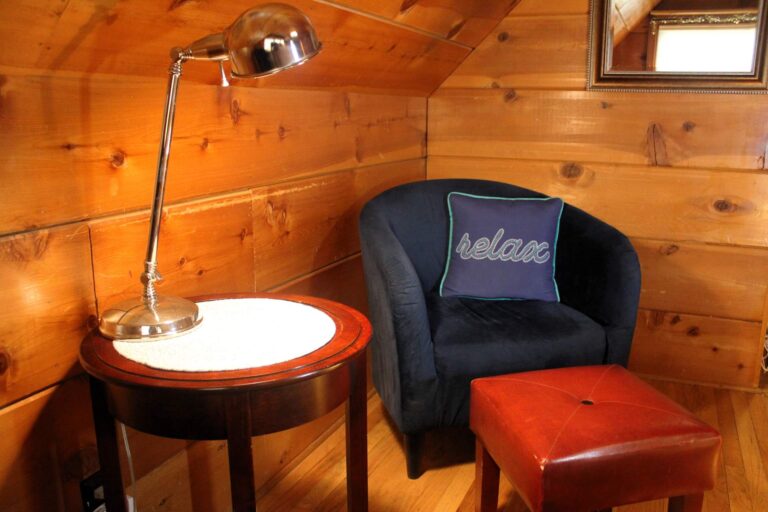 A deep blue velvet chair with a cursive 'relax' accent pillow paired with a red leather footstool.