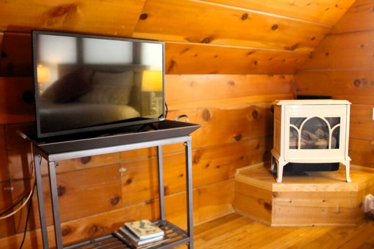 Flat-screen television on a metal media stand next to a vintage-style white freestanding gas fireplace stove.