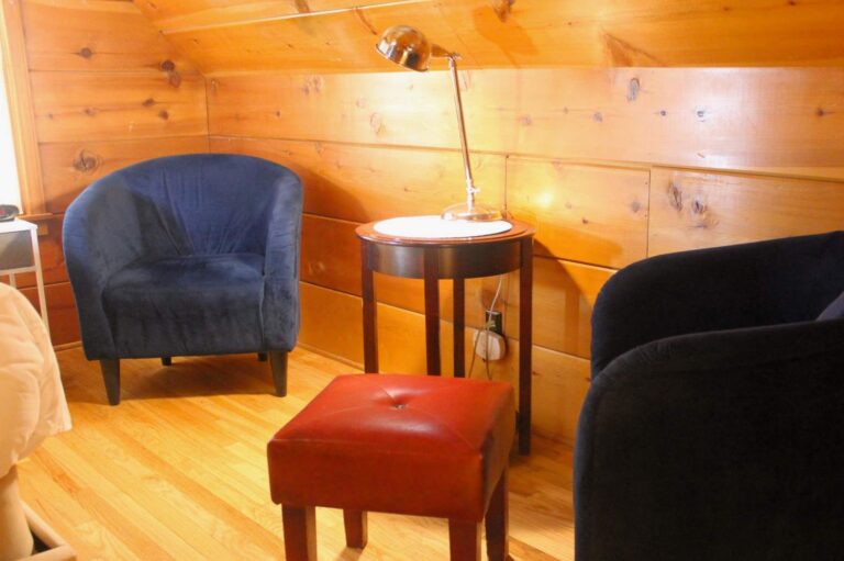 Two dark blue velvet tub chairs and a red leather footstool around a small wooden table in a pine-walled suite.