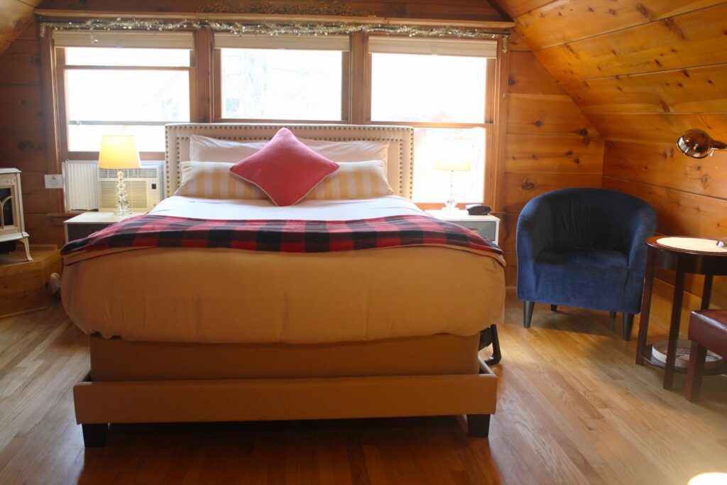 A queen bed with a red buffalo plaid blanket and an upholstered studded headboard inside the Dogwood Suite.