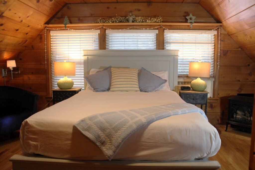Luxury bed with blue pillows and a plaid blanket under a vaulted knotty pine ceiling in the Sugar Pine Suite.