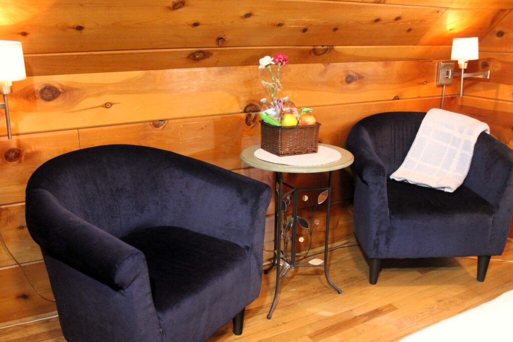 Two dark velvet accent chairs on polished hardwood floors in a rustic pine-walled guest suite.