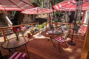 Home Spacious wooden guest deck at Shaver Lake Inn with umbrella-shaded patio tables and a massive boulder in the background.