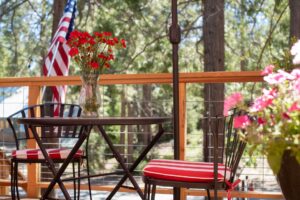 Close-up of a patio table with red flowers on a wooden guest deck at Shaver Lake Inn, surrounded by pine trees.