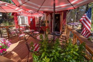 Home Outdoor wooden deck at Shaver Lake Inn featuring red and white umbrellas, patio tables, and a mountain forest backdrop.