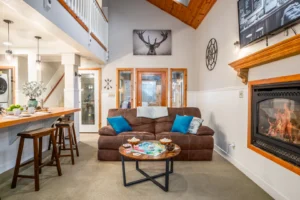 Open living area with a brown sofa, lit gas fireplace, board games on the coffee table, and an adjacent kitchen counter at Alpine Retreat.