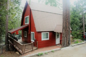 Exterior view of the red Bungalow on Buckeye A-frame cabin, showing the driveway, deck, and surrounding pine trees in Shaver Lake.