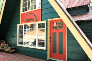 Front entrance of the green A-frame Four Seasons Chalet featuring a bright red door, large windows, and a wooden sign.